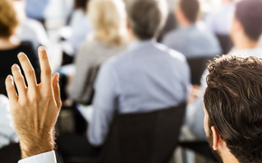 Die nächsten Veranstaltungen Mann hebt linke Hand zu einer Wortmeldung während einer Infoveranstaltung