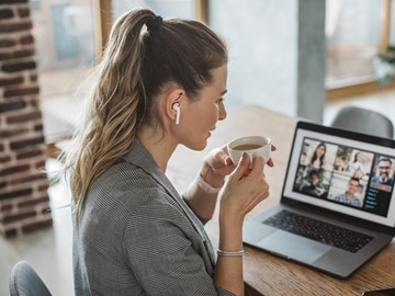Treffen Sie envia TEL auf einer unserer Veranstaltungen. Frau sitzt mit einer Tasse Kaffee vor Laptop und nimmt an einer Webkonferenz teil