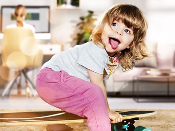 Privatkunden envia TEL Kind im Wohnzimmer sitzt auf einem Skateboard und streckt dabei die Zunge heraus