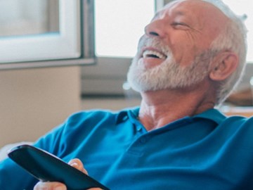 Highspeed für Zwenkau Mann und Frau sitzen gemeinsam auf einem Sofa und lachen, die Frau hält eine Fernbedienung in der Hand